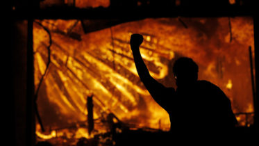 A protester gestures in front of the burning 3rd Precinct building of the Minneapolis Police Department.