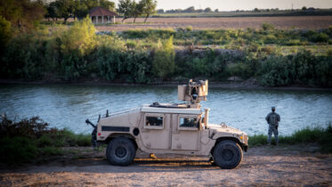 A National Guard member stands next to a tank by the Rio Grande river.