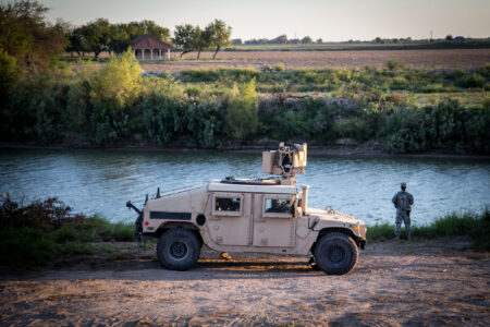 A National Guard member stands next to a tank by the Rio Grande river.