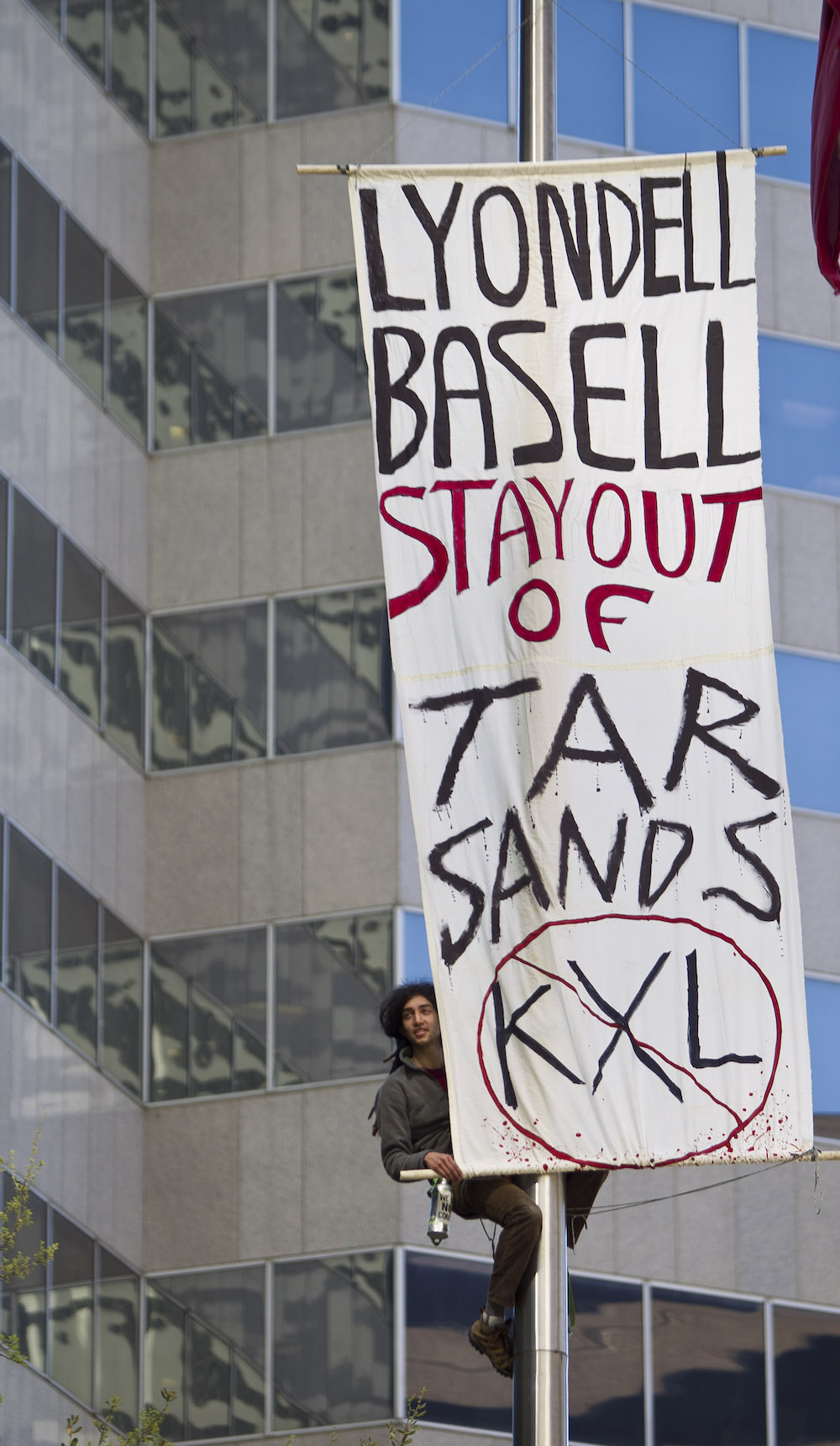 A protester on a flag poll with a sign that says 